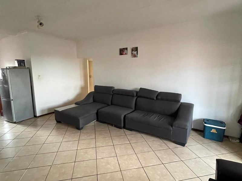 A spacious living area featuring neutral ceramic floor tiles and basic ceiling lighting, offering a blank canvas for potential interior updates.
