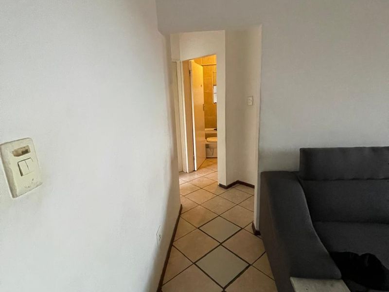 A narrow hallway with tiled flooring leading towards a bathroom, showing signs of wear on the walls and fixtures.