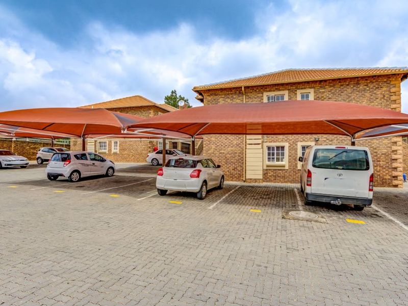 Exterior view of the apartment complex featuring brick facade buildings, paved parking area, and covered shade cloth carports.