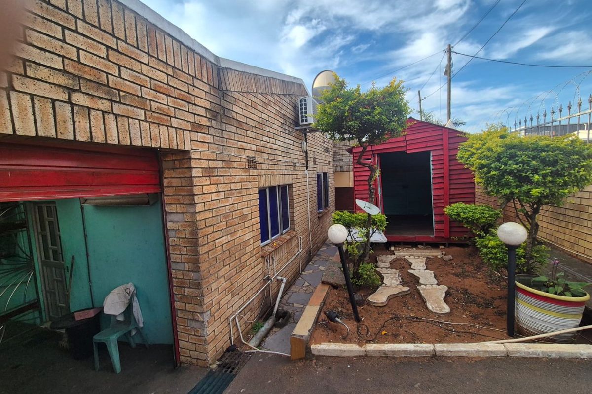 Rear exterior view featuring a face brick building, a red garden shed, and a small landscaped area with security fencing.