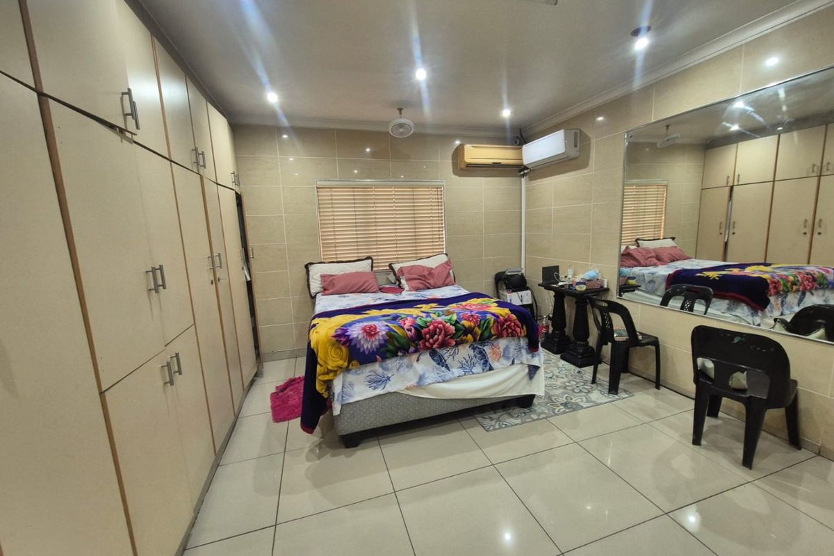 A bedroom featuring extensive built-in cabinetry, tiled walls and flooring, a wall-mounted air conditioning unit, and a large feature mirror.