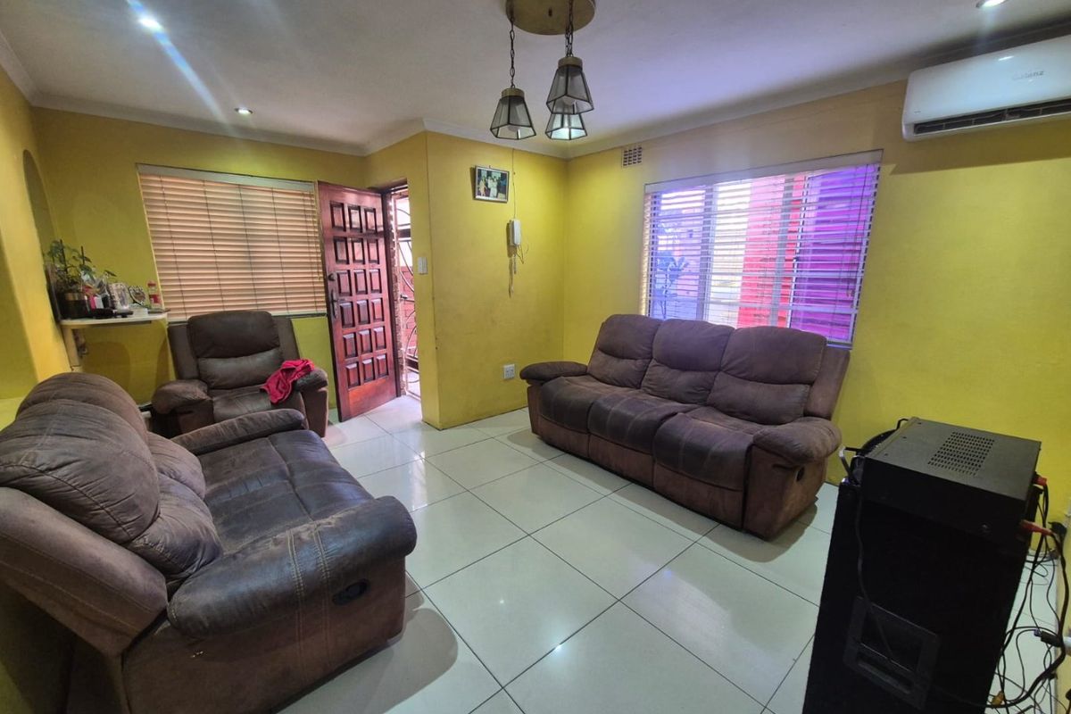 A living room featuring tiled flooring, an air conditioning unit, and natural light through venetian blinds, providing a functional and comfortable living space.