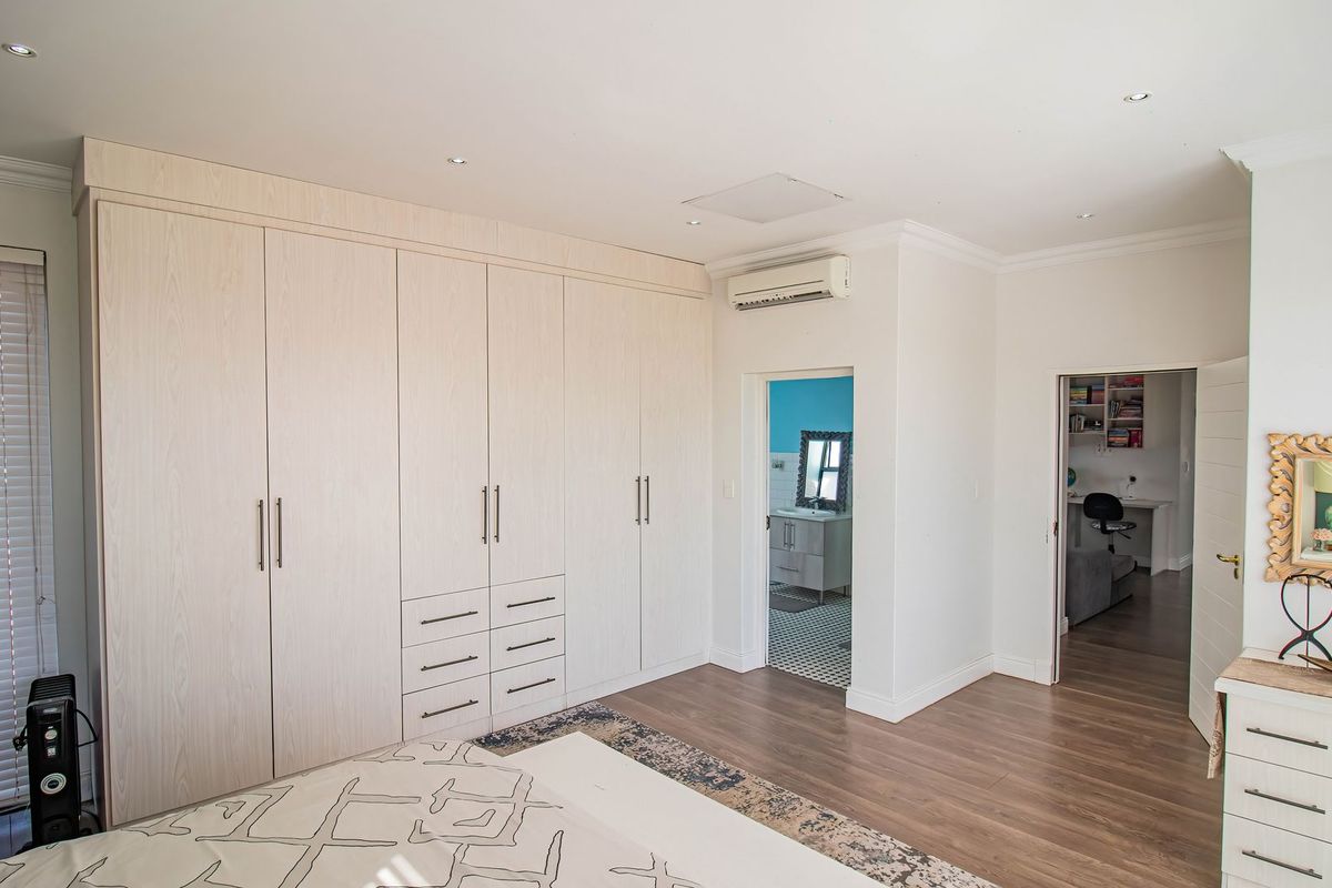 Spacious bedroom featuring extensive built-in cabinetry, laminate flooring, recessed lighting, and an integrated air conditioning unit, with direct access to an en-suite bathroom.