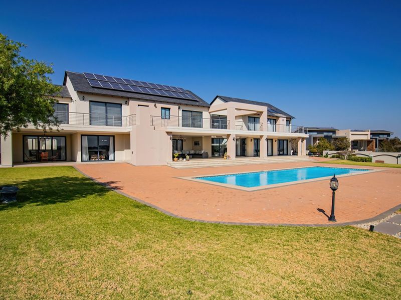 Spacious rear exterior featuring a large swimming pool, expansive paved patio, landscaped garden, and a multi-level residence equipped with solar panels.