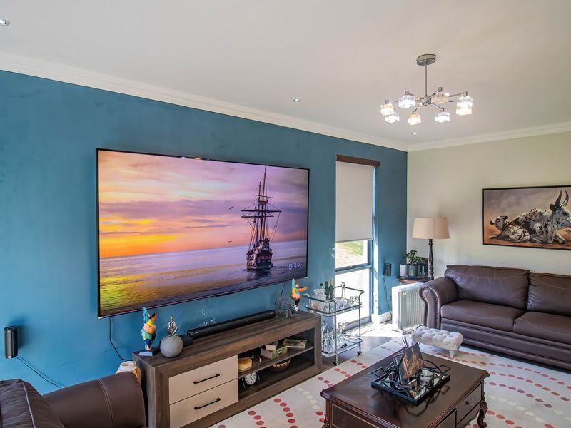 A comfortable living room featuring a bold blue accent wall, recessed lighting, and a modern chandelier, providing a cozy space for relaxation.