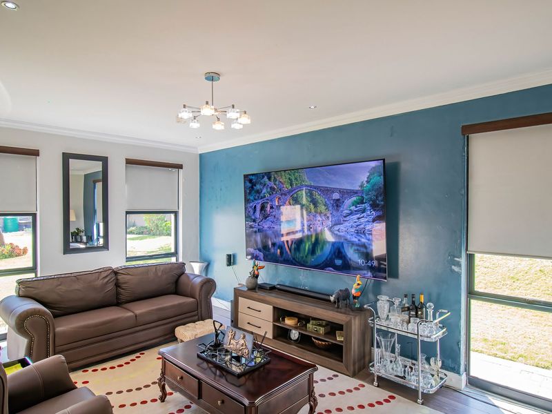 A well-lit living room featuring a bold blue accent wall, large windows with roller blinds, and recessed ceiling lighting.