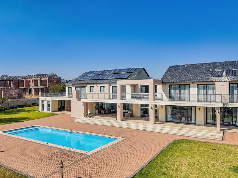 Spacious rear elevation of a modern two-story house featuring a large swimming pool, expansive paved patio, upper-level balcony, and integrated solar panels.