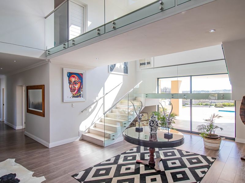 Spacious double-volume entrance hall featuring a modern glass staircase, sleek laminate flooring, and large sliding doors leading to the outdoor area.
