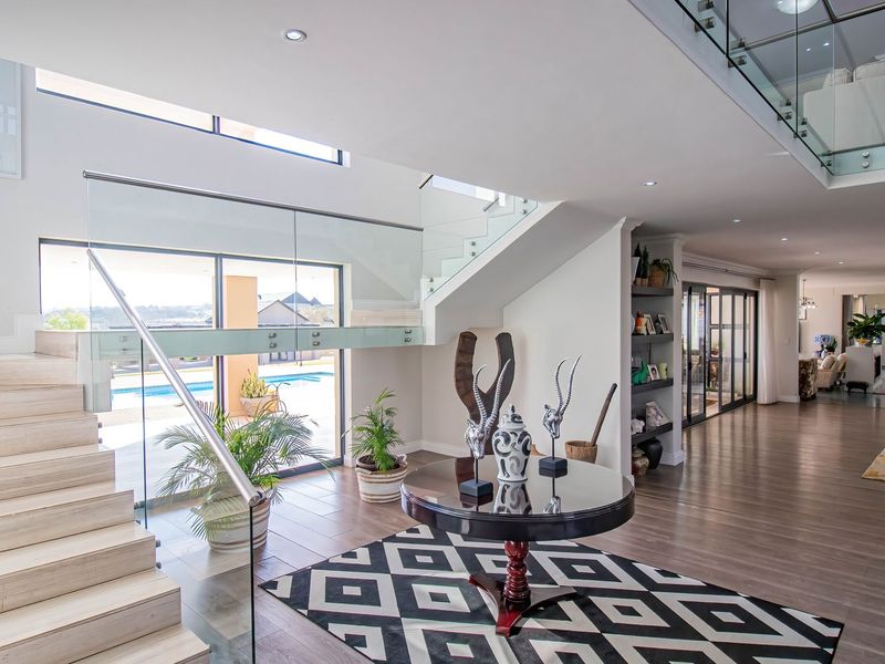 Spacious modern entrance hall featuring a striking timber staircase with glass balustrade, recessed lighting, and seamless flow to the outdoor pool area.