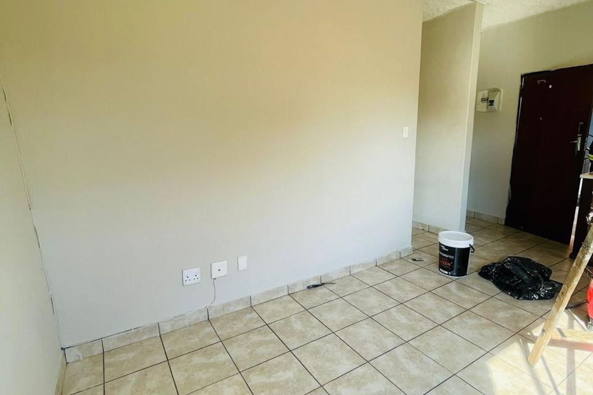 An empty living area featuring ceramic floor tiles, textured ceilings, and wall-mounted electrical points, currently undergoing minor maintenance.