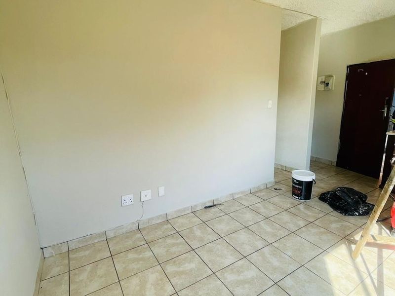 An empty living area featuring ceramic floor tiles, textured ceilings, and wall-mounted electrical points, currently undergoing minor maintenance.