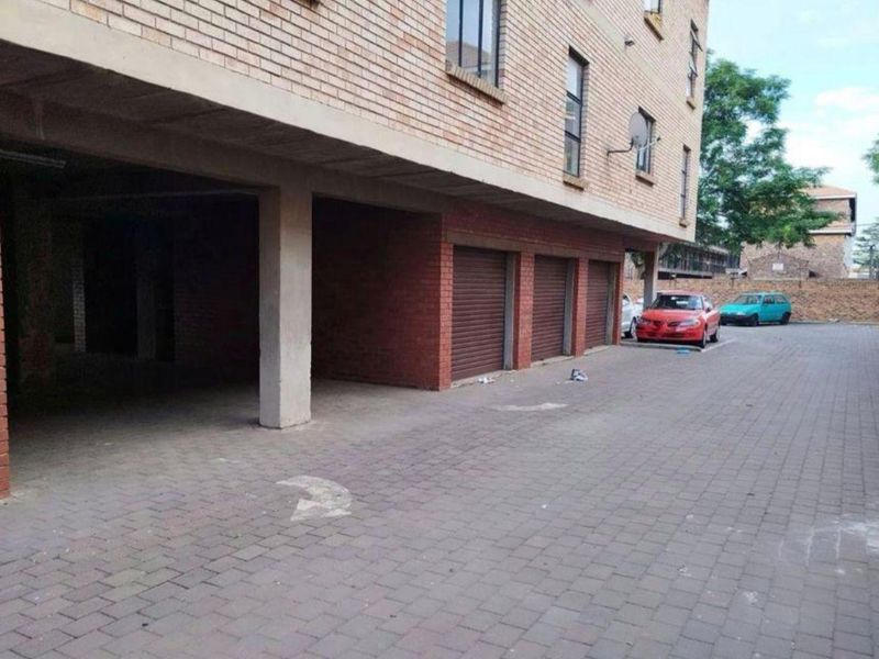 Ground level parking area featuring multiple roller shutter garage doors and paved driveway access within an apartment complex.