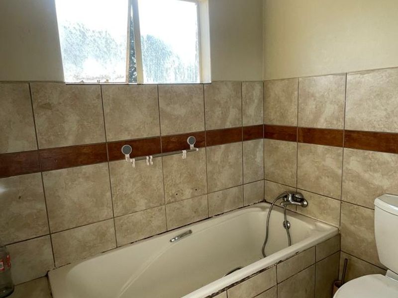 A dated bathroom featuring a built-in bathtub, ceramic tiling, and a standard toilet, requiring cosmetic updates to improve its overall condition and appeal.