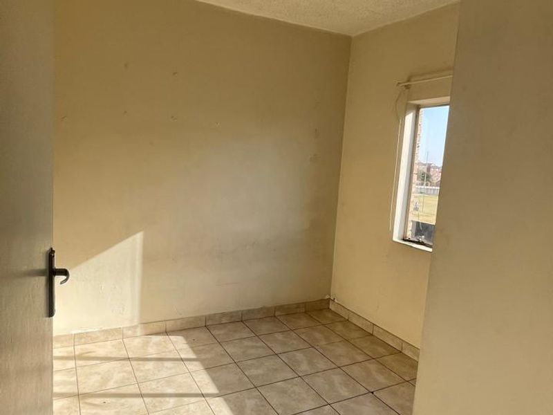 An empty bedroom featuring tiled flooring and a window, requiring cosmetic updates to the ceiling and flooring.