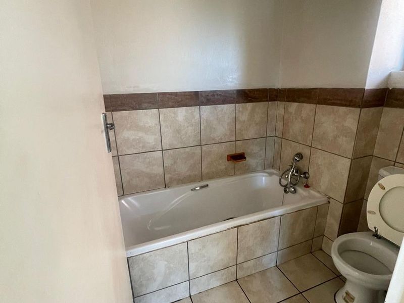 A functional bathroom featuring a built-in bathtub, toilet, and neutral ceramic tiling throughout the floor and walls.