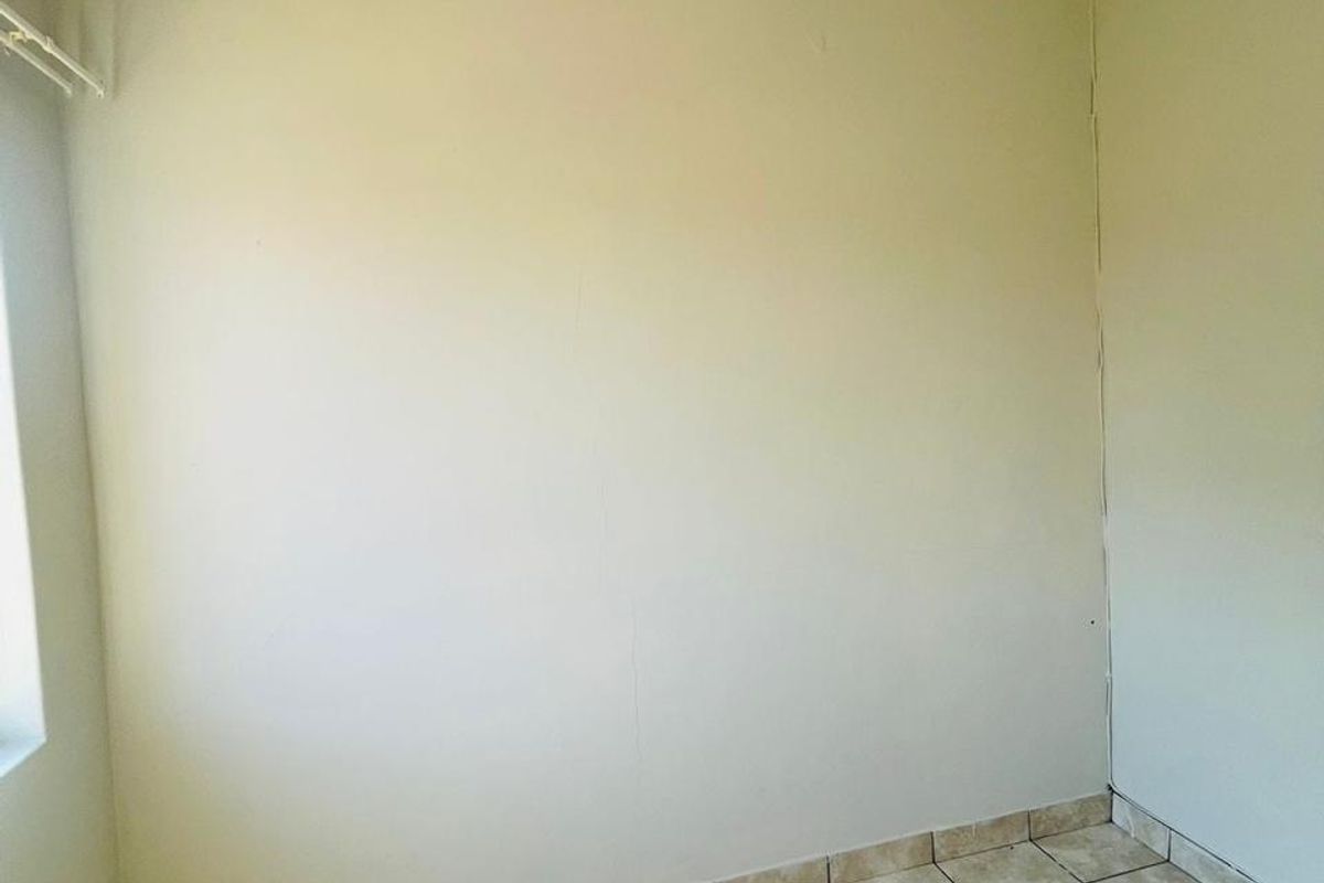 An empty bedroom featuring neutral wall paint and tiled flooring, requiring minor cosmetic repairs to the wall and ceiling finishes.
