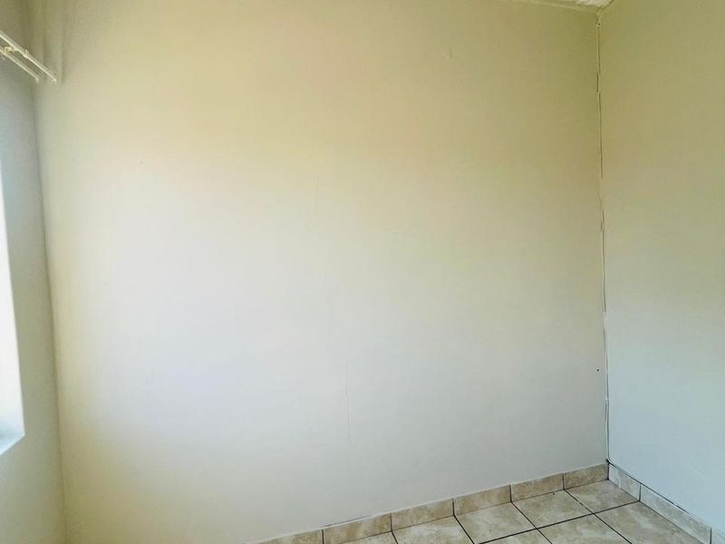 An empty bedroom featuring neutral wall paint and tiled flooring, requiring minor cosmetic repairs to the wall and ceiling finishes.
