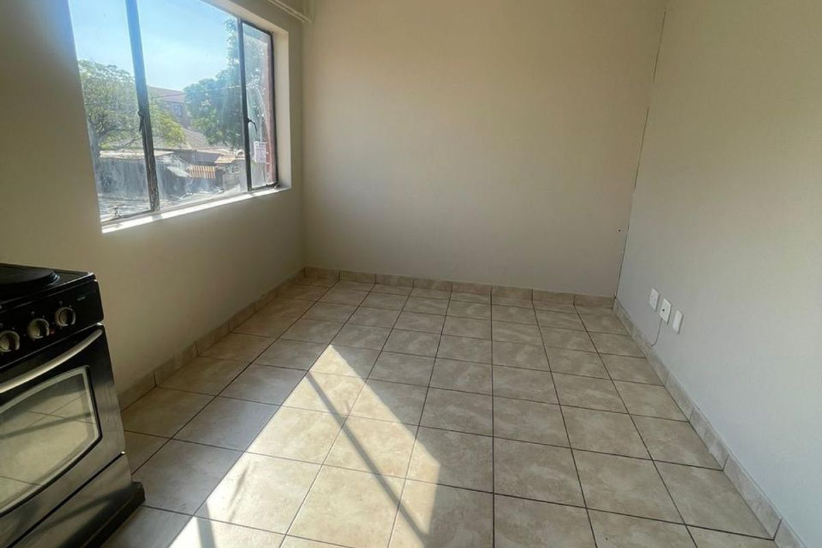 An empty kitchen area featuring tiled flooring and a freestanding stove, awaiting renovation or staging to maximize its potential.