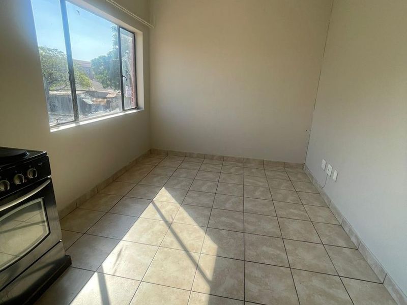 An empty kitchen area featuring tiled flooring and a freestanding stove, awaiting renovation or staging to maximize its potential.