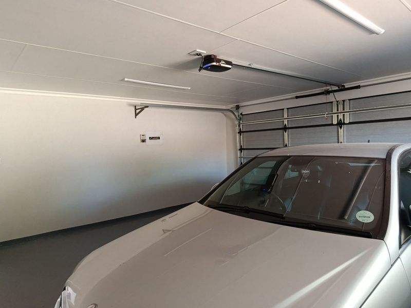 A clean and well-maintained garage featuring an automated sectional door, epoxy flooring, and integrated lighting.