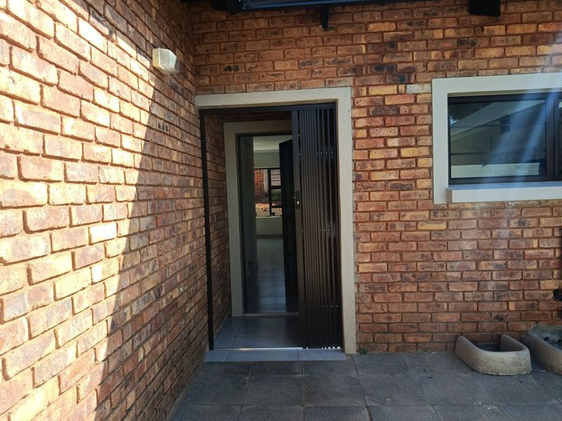 Exterior view of the home entrance featuring face brick walls, a security gate, and a tiled patio area.