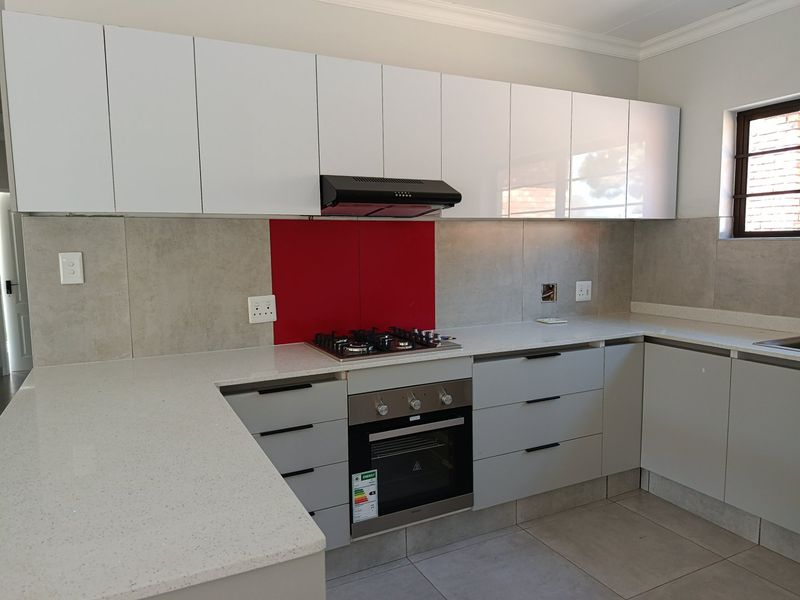 Modern kitchen featuring white upper cabinetry, grey lower drawers, stone countertops, gas hob, built-in oven, and a red feature splashback.