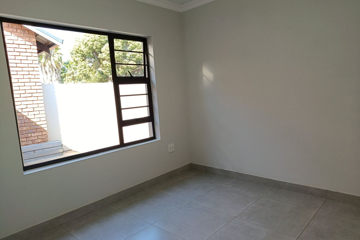 A clean, empty bedroom featuring neutral tiled flooring, fresh paint, and a large aluminium-framed window providing natural light.