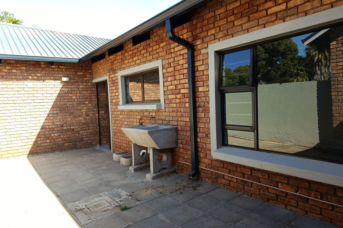 Rear exterior view of the property featuring exposed brick walls, a paved patio area, and a functional concrete utility sink.