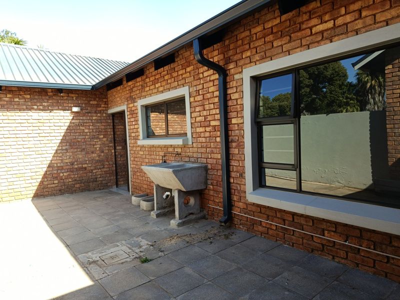 Rear exterior view of the property featuring exposed brick walls, a paved patio area, and a functional concrete utility sink.