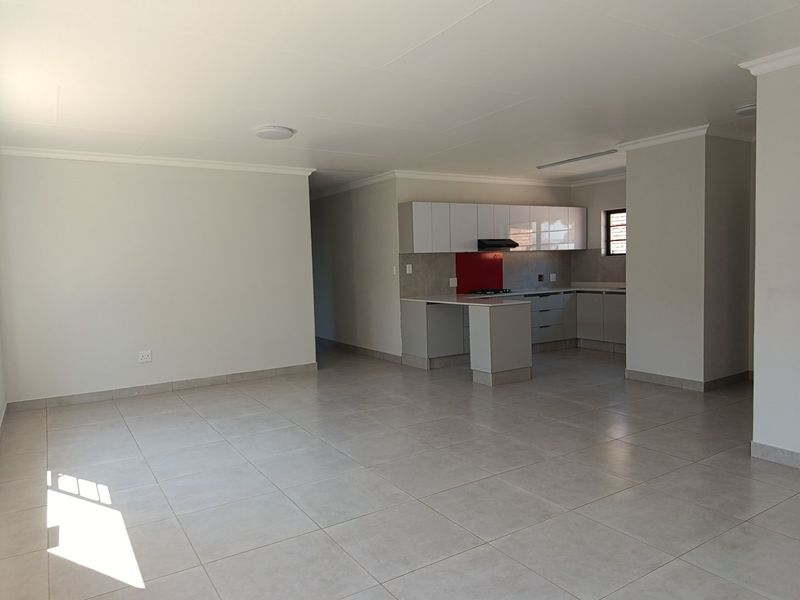 Spacious open-plan living area featuring neutral tiled flooring and a modern kitchen with built-in cabinetry, peninsula, and a red tiled backsplash.