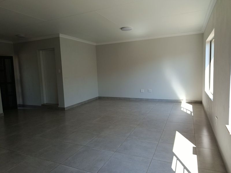 A spacious, empty living area featuring neutral tiled flooring, coved ceilings, and natural light from a side window.