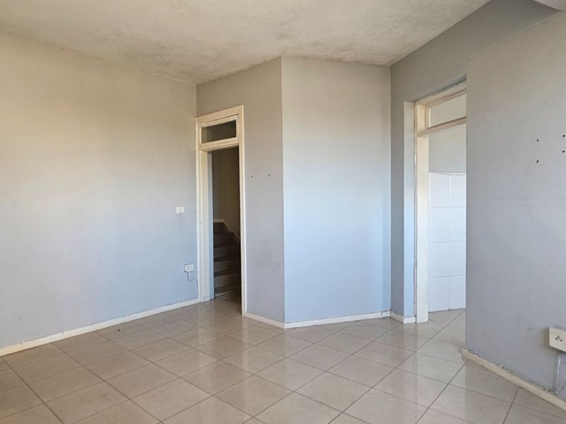 An empty living room featuring neutral tiled flooring and light grey walls, providing a blank canvas for potential interior design and renovation.