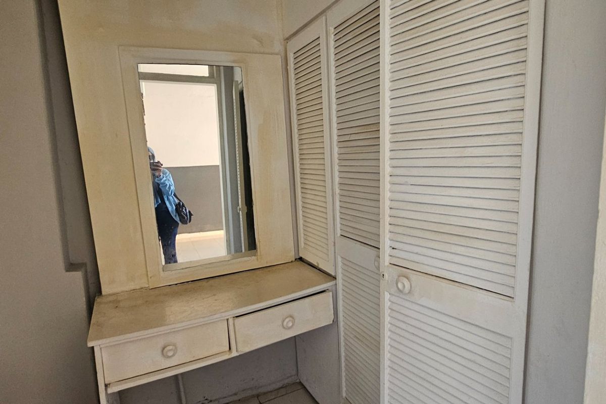 A bedroom area featuring a built-in vanity with a mirror and integrated louvered wardrobe cabinetry, showing signs of wear and aging.