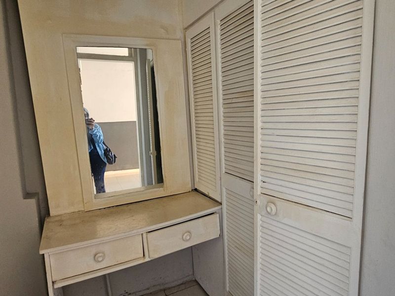 A bedroom area featuring a built-in vanity with a mirror and integrated louvered wardrobe cabinetry, showing signs of wear and aging.