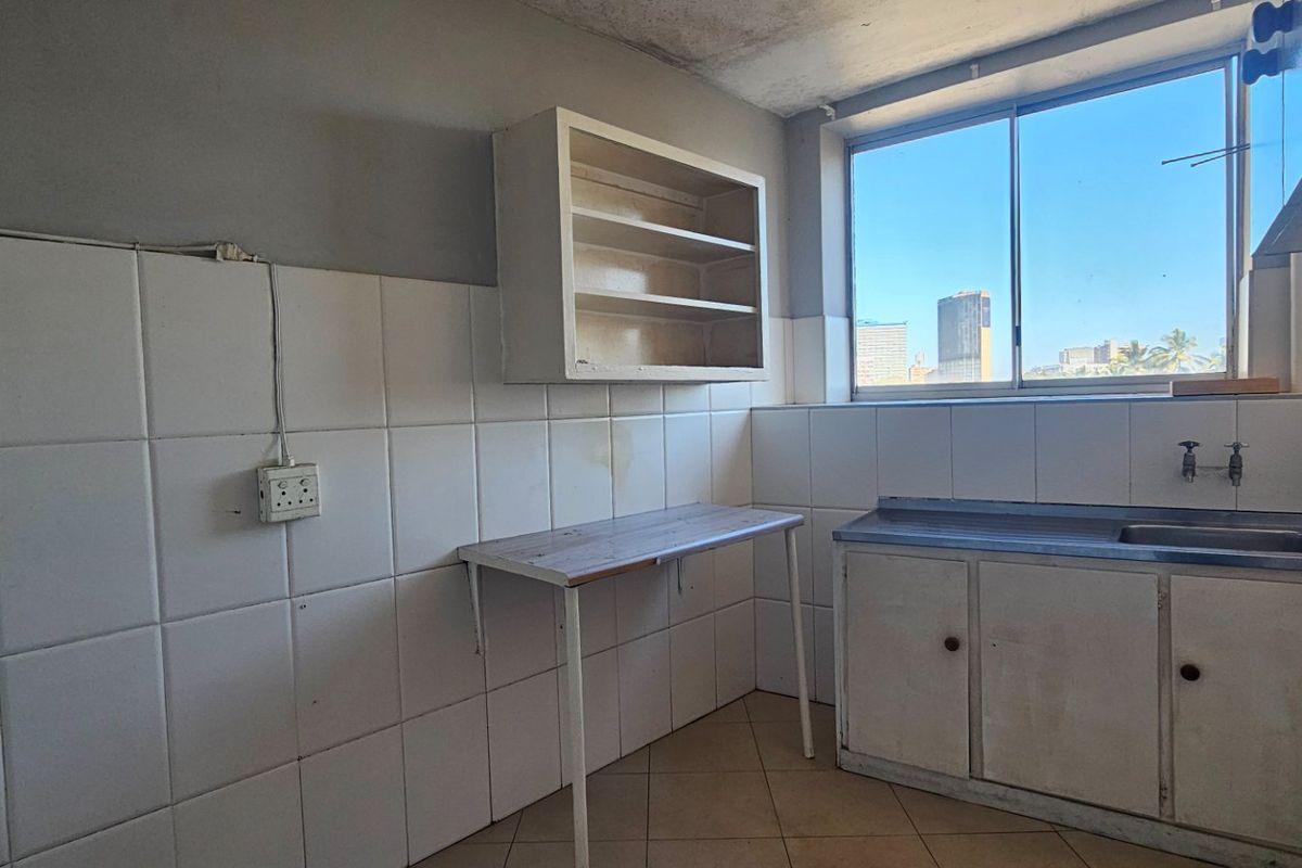 A dated, empty kitchen featuring tiled walls, a basic sink unit, and wall-mounted shelving, offering a blank canvas for renovation.