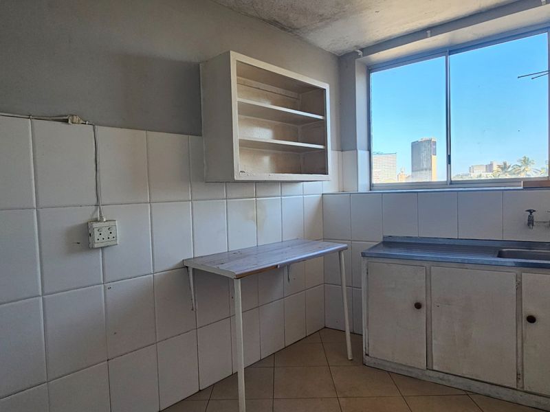 A dated, empty kitchen featuring tiled walls, a basic sink unit, and wall-mounted shelving, offering a blank canvas for renovation.