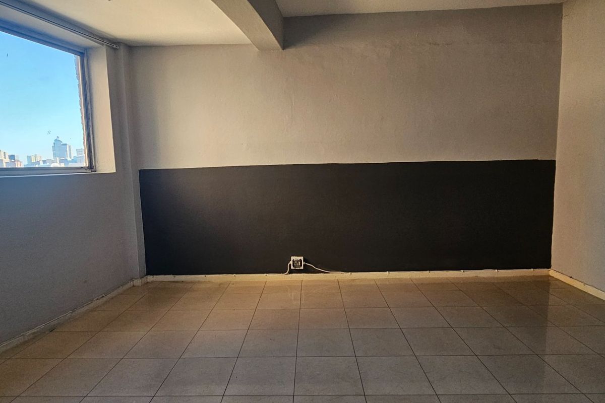 An empty living room featuring tiled flooring, a large window with city views, and a two-tone painted wall finish.