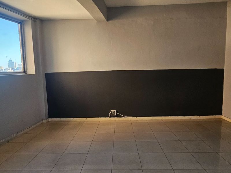 An empty living room featuring tiled flooring, a large window with city views, and a two-tone painted wall finish.