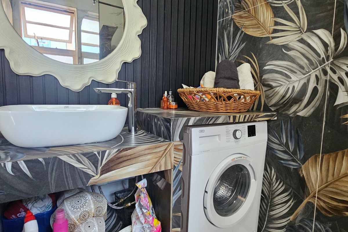 A modern bathroom featuring a vessel sink, custom vanity with integrated washing machine, and decorative botanical wall tiling.