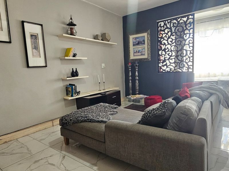 A living room featuring marble-look floor tiles, floating wall shelves, and a decorative laser-cut room divider, creating a modern open-plan feel.