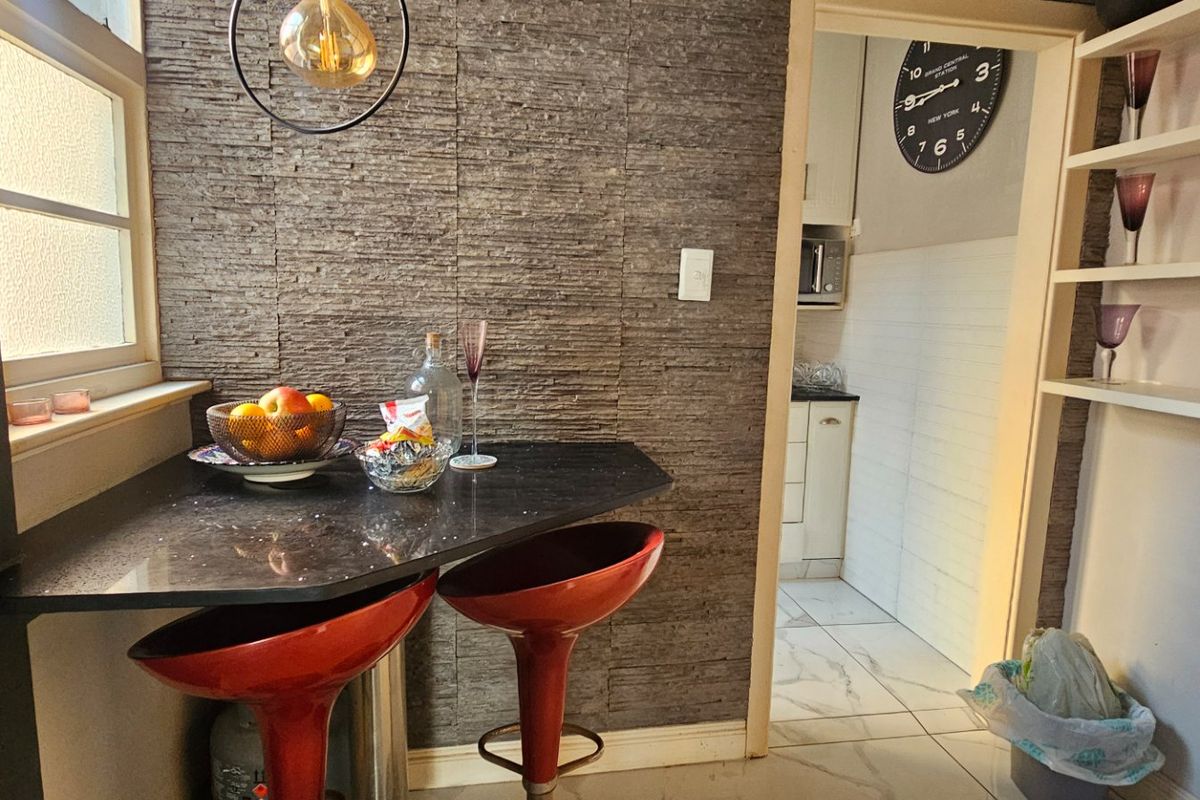 A compact kitchen area featuring a stone veneer accent wall, a built-in breakfast bar, and marble-look floor tiles, leading into a functional kitchen space.
