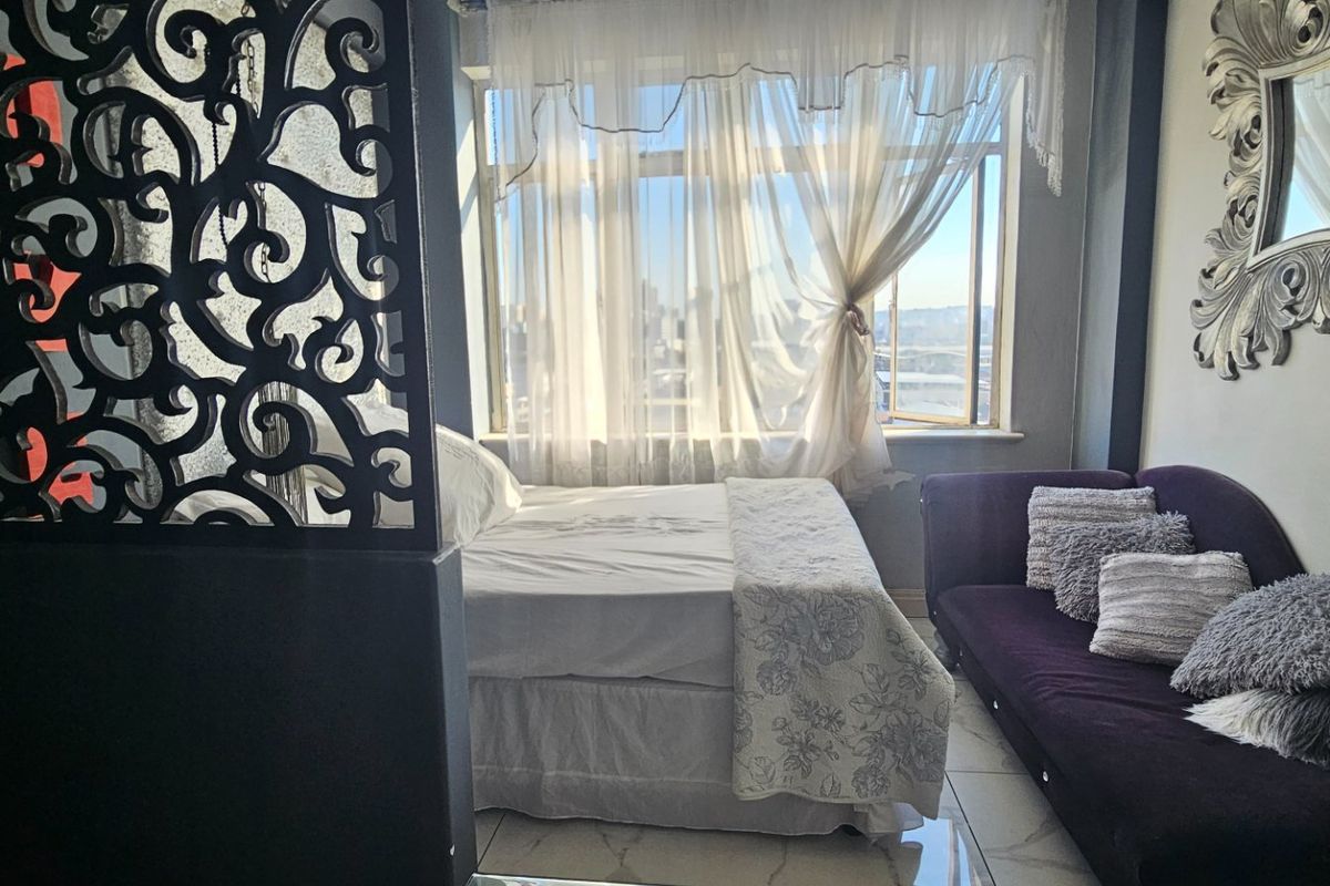 A bedroom featuring tiled flooring, a large window allowing natural light, and a decorative room divider creating a distinct sleeping area.