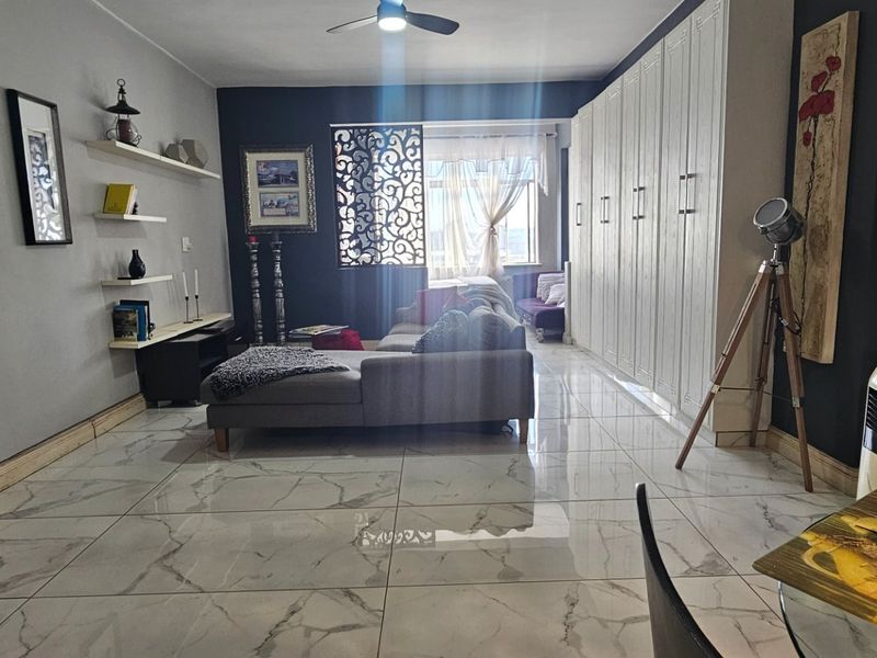 A living room featuring large format marble-look floor tiles, built-in floor-to-ceiling cabinetry, and a ceiling fan.