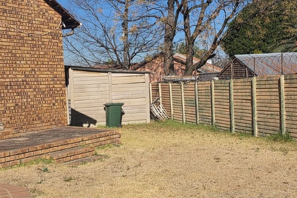 Rear garden area featuring a brick facade, concrete patio, and perimeter boundary wall with security fencing.