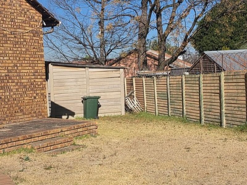 Rear garden area featuring a brick facade, concrete patio, and perimeter boundary wall with security fencing.