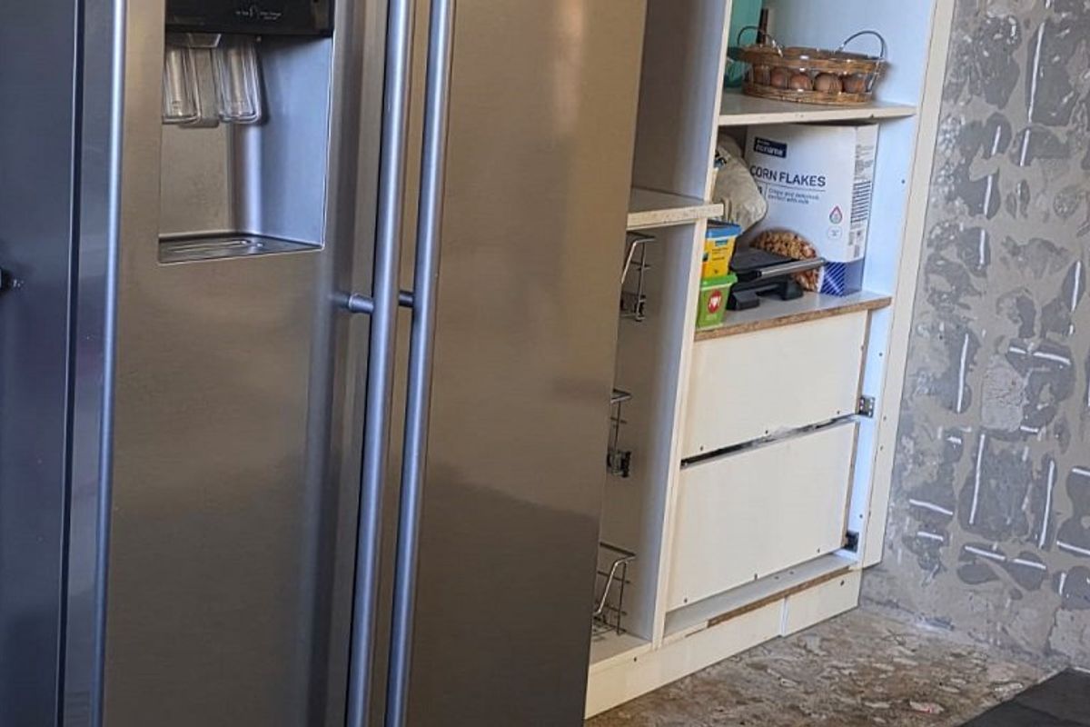 A kitchen area featuring built-in cabinetry and shelving, currently showing unfinished wall surfaces requiring repair and completion.