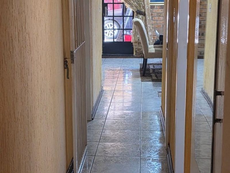A narrow hallway featuring tiled flooring and textured walls, leading towards an exterior door.