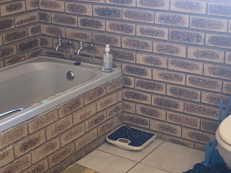 A bathroom featuring exposed brick walls, a built-in bathtub, and ceramic floor tiles, offering potential for a modern renovation.