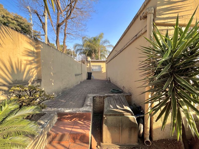 A narrow rear exterior walkway featuring paved flooring, boundary walls with electric fencing, and tiled steps leading to the side of the property.