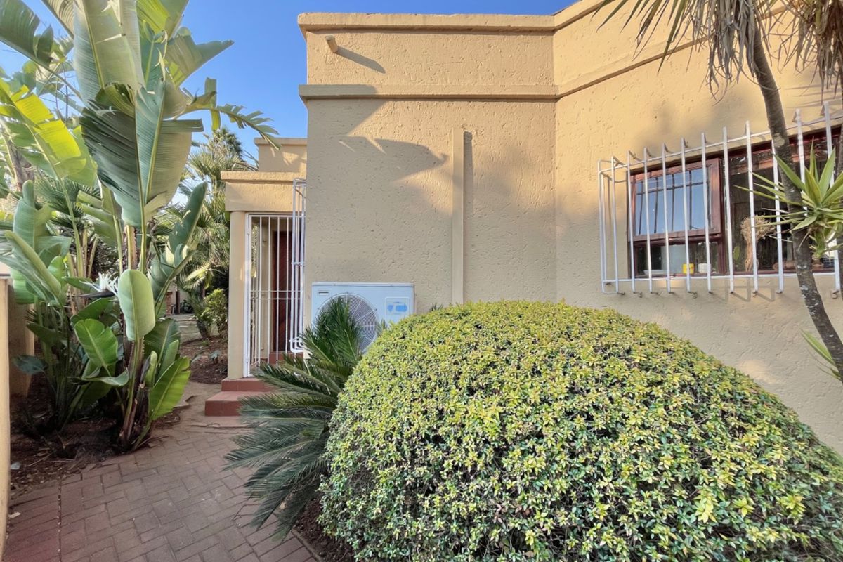 Rear exterior view of the property featuring a paved walkway, stucco wall finish, security bars on windows, and an external air conditioning unit.